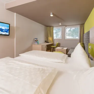 Köpfle Modern hotel room with double bed, wall-mounted TV, desk, and sofa seating area